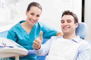 Patient sitzt neben Zahnarzt und hält Daumen hoch